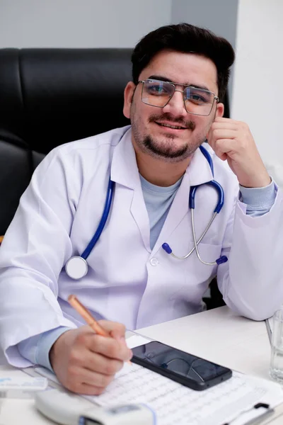 Mladý Doktor Sedí Klinice Drží Pero Ruce Usmívá — Stock fotografie