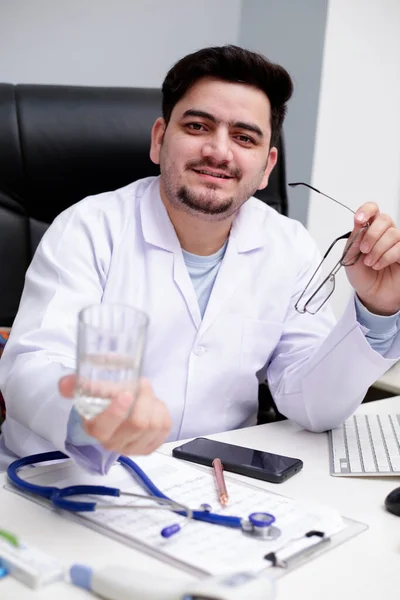 Młody Lekarz Siedzi Klinice Trzymając Szklankę Wody Ręce — Zdjęcie stockowe