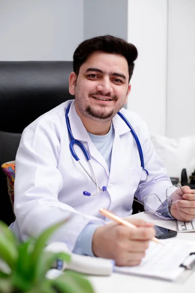 Jovem Médico Está Sentado Clínica Segurando Mão Caneta Sorrindo — Fotografia de Stock