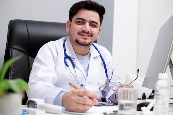 Joven Médico Está Sentado Clínica Con Mano Pluma Sonriendo — Foto de Stock