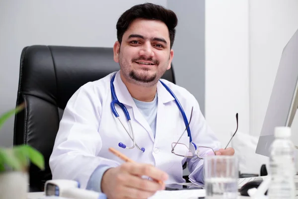 Joven Médico Está Sentado Clínica Con Mano Pluma Sonriendo — Foto de Stock