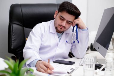 Klinikte elinde steteskop olan genç bir doktor oturmuş gazete okuyor..