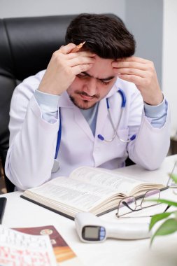 Genç bir doktor klinikte oturmuş günlükten bir şeyler okuyor ve yorgun hissediyor..