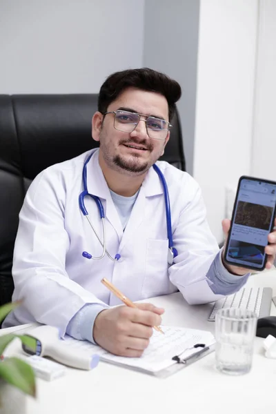 Jovem Médico Está Sentado Clínica Segurando Móvel Mão Mostrando Algo — Fotografia de Stock