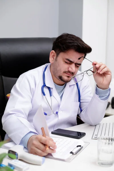 Młody Lekarz Siedzi Klinice Trzymając Okulary Dłoni Czuje Się Zmęczony — Zdjęcie stockowe