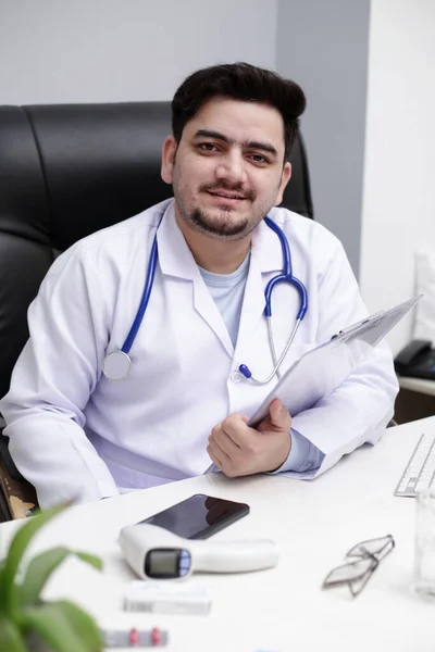 Joven Médico Está Sentado Clínica Sosteniendo Informe Gráfico Mano Sonriendo —  Fotos de Stock