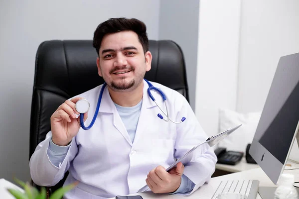 Jovem Médico Está Sentado Clínica Segurando Estetoscópio Mão Sorrindo — Fotografia de Stock