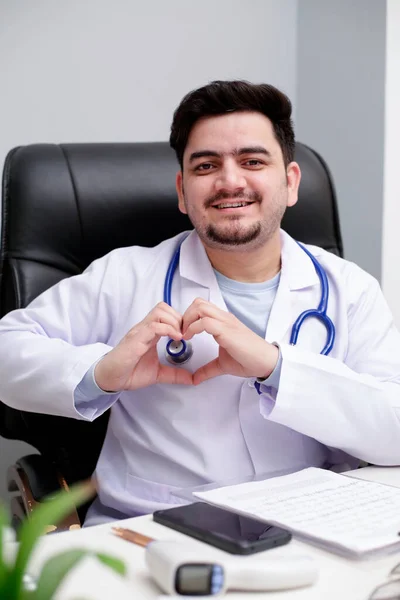 Médico Joven Está Sentado Clínica Haciendo Corazón Con Mano Sonriendo —  Fotos de Stock
