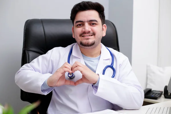 Médico Joven Está Sentado Clínica Haciendo Corazón Con Mano Sonriendo — Foto de Stock