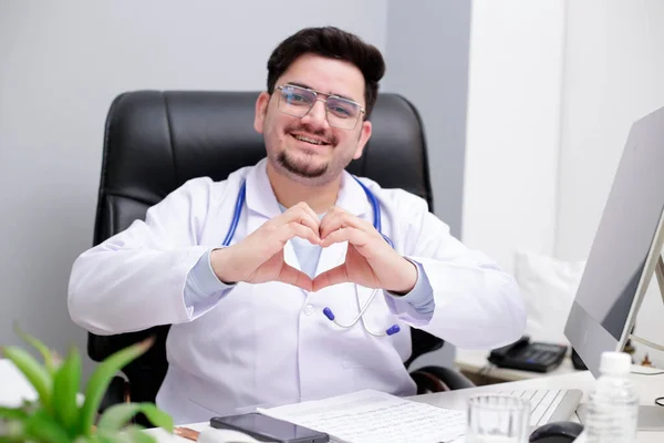 Jovem Médico Está Sentado Clínica Fazendo Coração Com Mão Sorrindo — Fotografia de Stock