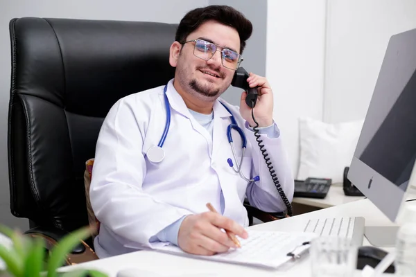 Młody Lekarz Siedzi Klinice Rozmawia Przez Telefon Uśmiecha Się — Zdjęcie stockowe