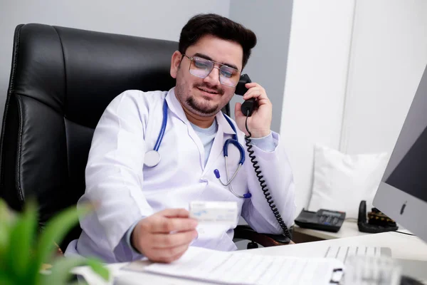 Młody Lekarz Siedzi Klinice Rozmawia Przez Telefon Trzyma Leki Ręku — Zdjęcie stockowe
