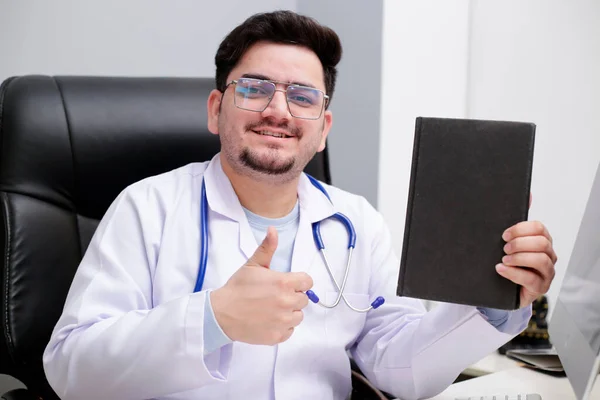 Médico Joven Está Sentado Clínica Sosteniendo Diario Mano Mostrando Cartel —  Fotos de Stock