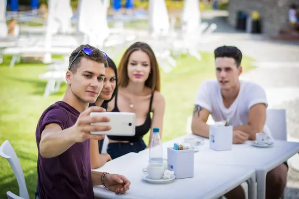 Young handsome men and attractive women smiling sitting at table making selfie.