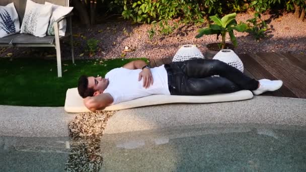 一个英俊的年轻人在游泳池边放松 躺在地上的一个床垫上 — 图库视频影像