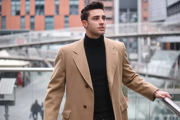 Handsome young man walking in trendy trench coat through city street. Confident young man walking in fashionable trench coat in city street.