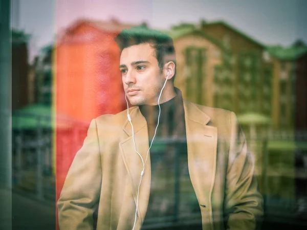 A man with earphones standing in front of a window