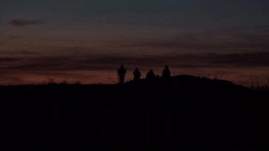 Gün batımında bir dağda el ele yürüyen bir grup insan.