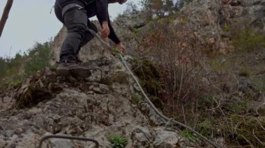 Orta yaşlı bir adam güneşli bir sonbahar gününde ferrata / klettersteig üzerinden kayaya tırmanıyor.