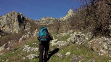 Sırt çantalı aktif bir adam dağın eteğindeki kayalık çayırlarda yürüyüş yapıyor.