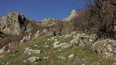 Sırt çantalı aktif bir adam dağın eteğindeki kayalık çayırlarda yürüyüş yapıyor.