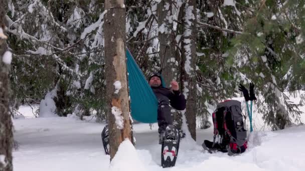 冬の森の木々の下にハンモックに寝そべっているスノーシューのハイカー リラックスした男 冬のキャンプ — ストック動画