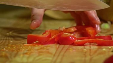 Ahşap tahtada mutfakta kırmızı biberi kesen kadın elleri. Kapatın. Yavaş çekim.