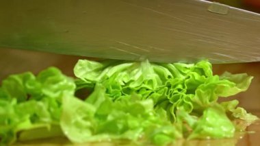 Ahşap tahtada mutfakta marulu kesen kadın elleri. Kapatın. Yavaş çekim.