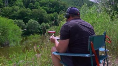 Alıştırma pedleri ve kulaklıkları olan bir sanatçı, dağ gölü yakınlarında açık havada pratik yapıyor. Davul çalışması