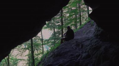 Yürüyüşçü bir mağarada mola verir ve dışarıda, doğada kitap okur.