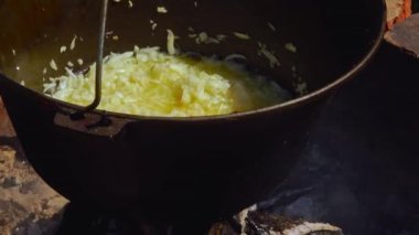 Geleneksel bir Romen yemek sahnesinde, otantik zakuska yapımında önemli bir adım olarak, odun ateşinin üzerinde soğan soteleniyor. Kırsal açık hava düzeni, bu lezzetli yayılımı yaratmak için kullanılan onurlu yöntemleri vurgular..