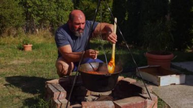 Geleneksel Romen zakuskasının ahşap bir ateşin üzerinde bir kazanda hazırlandığını gösteren kırsal bir sahne. Bu açık hava pişirme süreci doğal malzemelerin ve geleneksel yöntemlerin kullanımını vurguluyor ve bu da zengin ve lezzetli bir yayılımla sonuçlanıyor..