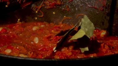 Geleneksel bir Romen yemek anı, baharatların odun ateşinin üzerinde kaynayan bir zakuska kazanına eklendiği. Bu rustik açık hava sahnesi lezzetlerin aromatik karışımını yakalar ve bu otantik yemeği yapma sürecini gözler önüne serer..