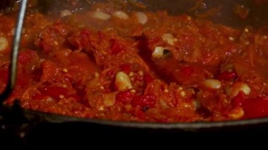 Geleneksel Romen zakuskasının ahşap bir ateşin üzerinde bir kazanda hazırlandığını gösteren kırsal bir sahne. Bu açık hava pişirme süreci doğal malzemelerin ve geleneksel yöntemlerin kullanımını vurguluyor ve bu da zengin ve lezzetli bir yayılımla sonuçlanıyor..