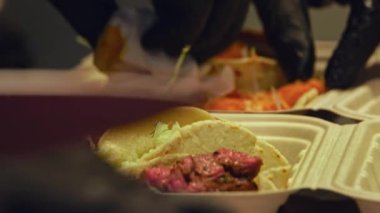 Izgara sığır eti ve taze salatanın dikkatlice paketlenip bu yakın çekim videoda teslim edilmeye hazır hale getirilmesini izleyin. Yumuşak, sulu sığır eti, yumuşak ekmeğe sarılmış, canlı, gevrek bir salata ile eşleştirilir..