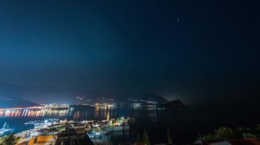 Budva 'nın aydınlanmış eski kenti ve marinası üzerinde tekneli, Karadağ' ın açık bir gece gökyüzünün inanılmaz hızlandırılmış videosu.
