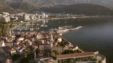 Drone flight over the city of Budva in Montenegro, old town, houses with red roofs and marina with boats.