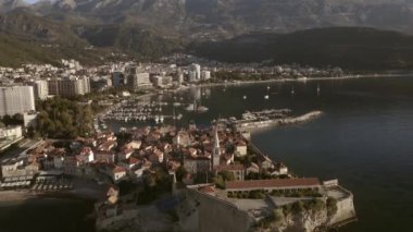 Drone flight over the city of Budva in Montenegro, old town, houses with red roofs and marina with boats.