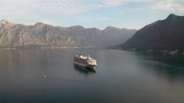 Aerial video of a large cruise ship passing near the beautiful city of Perast and leaving the picturesque bay of Kotor (Boka Kotor) in Montenegro