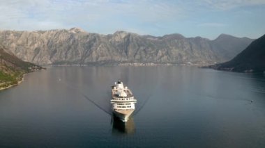 Aerial video of a large cruise ship passing near the beautiful city of Perast and leaving the picturesque bay of Kotor (Boka Kotor) in Montenegro