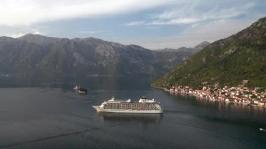 Aerial video of a large cruise ship passing near the beautiful city of Perast and leaving the picturesque bay of Kotor (Boka Kotor) in Montenegro
