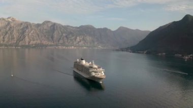 Aerial video of a large cruise ship passing near the beautiful city of Perast and leaving the picturesque bay of Kotor (Boka Kotor) in Montenegro