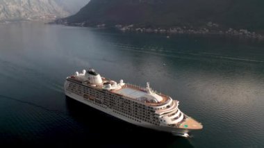Aerial video of a large cruise ship passing near the beautiful city of Perast and leaving the picturesque bay of Kotor (Boka Kotor) in Montenegro