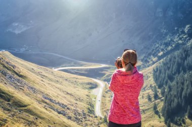 Bir uçurumun tepesindeki genç bir kadının arka görüntüsü Romanya 'daki ünlü Transfagarasan dağ yolunun muhteşem panoramik manzarasını çekiyor.