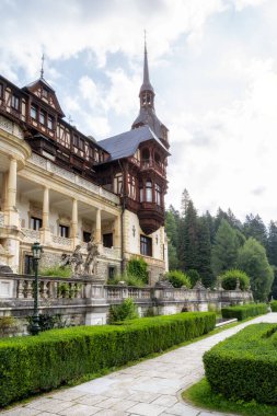 Romanya 'nın Sinaia kenti yakınlarındaki Peles Kalesi' nin güzel cephesinin önündeki bahçedeki heykeller ve bitkiler.