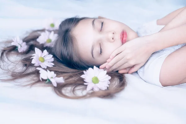 一个美丽的高加索女孩睡在白色长发上 开着雏菊花 用柔和的色调把画像拍了下来 — 图库照片