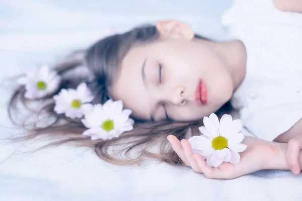 一个美丽的高加索女孩睡在白色长发上 开着雏菊花 用柔和的色调把画像拍了下来 — 图库照片