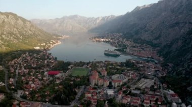 Kotor 'un (Boka Kotor) güzel kıyı şeridi, kırmızı çatıları, tekneli marinası ve Karadağ' daki büyük yolcu gemisi.