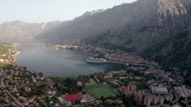 Kotor 'un (Boka Kotor) güzel kıyı şeridi, kırmızı çatıları, tekneli marinası ve Karadağ' daki büyük yolcu gemisi.