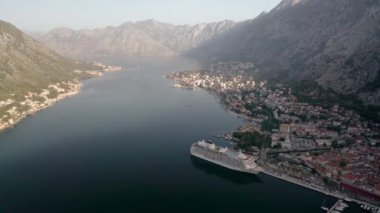 Kotor 'un (Boka Kotor) güzel kıyı şeridi, kırmızı çatıları, tekneli marinası ve Karadağ' daki büyük yolcu gemisi.